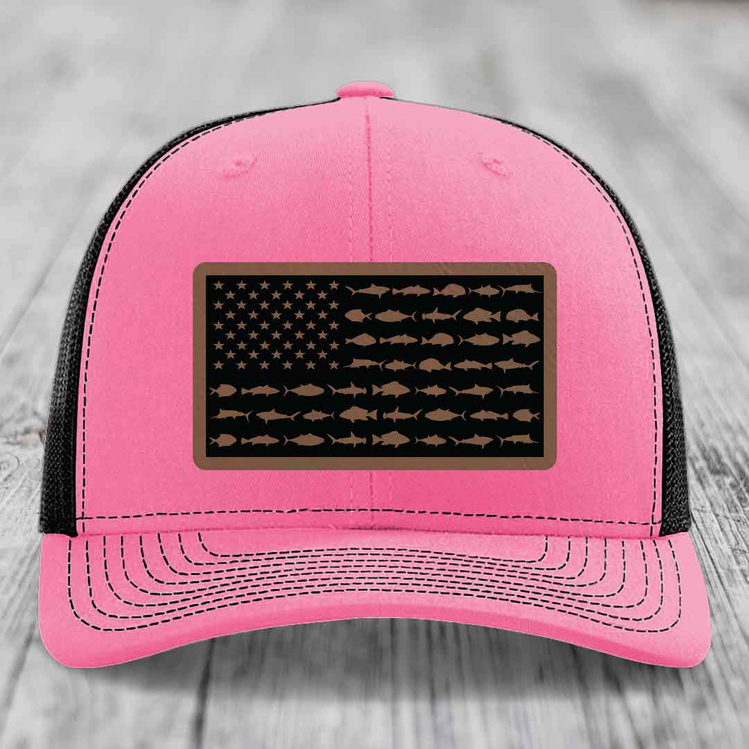 Pink trucker hat with black mesh back, featuring a rectangular leather patch with an American flag design made of fish silhouettes.