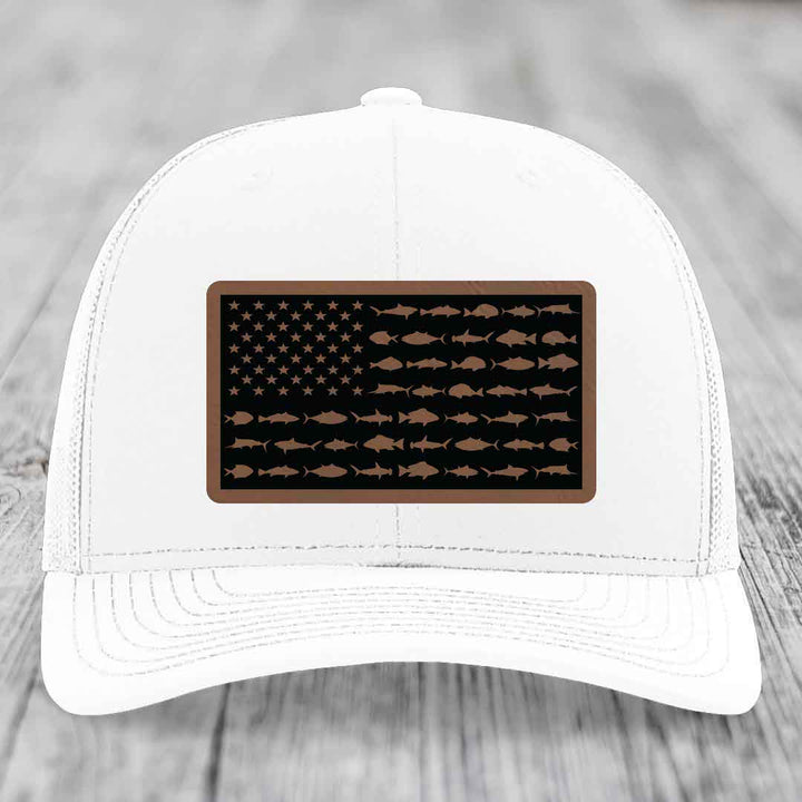 White trucker hat with a rectangular patch featuring an American flag design made of fish silhouettes in brown on a black background.