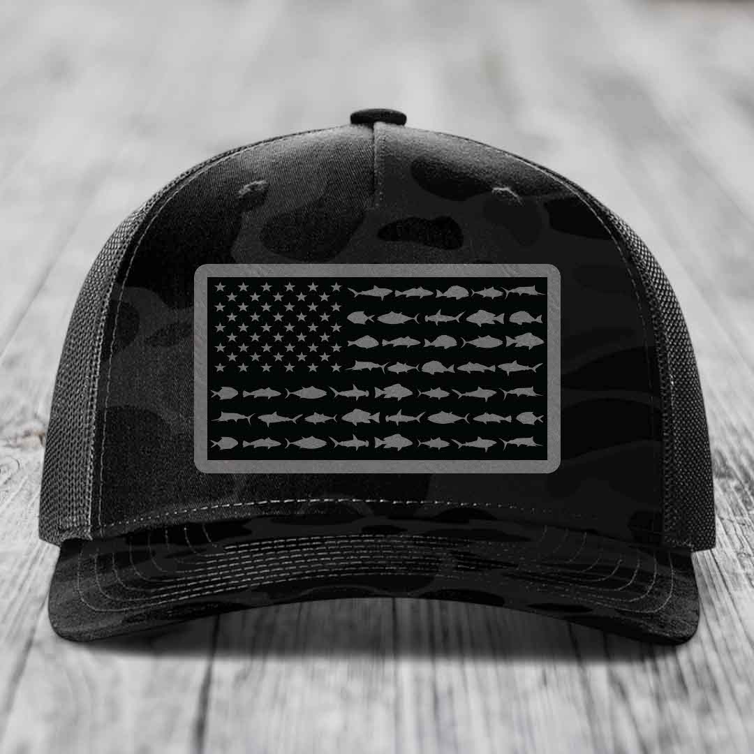 Black camouflage trucker hat with American flag patch made of saltwater fish silhouettes.