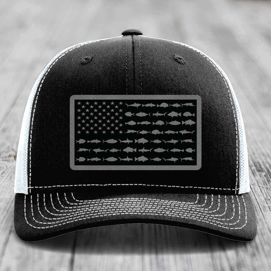 Black trucker hat with white stitching and a gray American flag patch made of saltwater fish silhouettes.