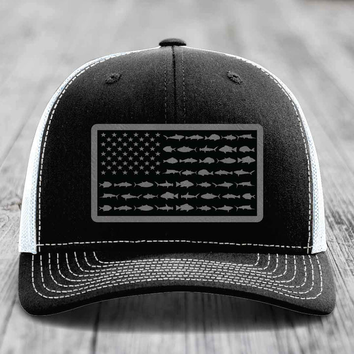 Black trucker hat with white stitching and a gray American flag patch made of saltwater fish silhouettes.