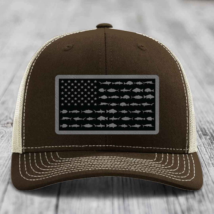 Brown trucker hat with white stitching and a black leather patch featuring an American flag design made of fish silhouettes.