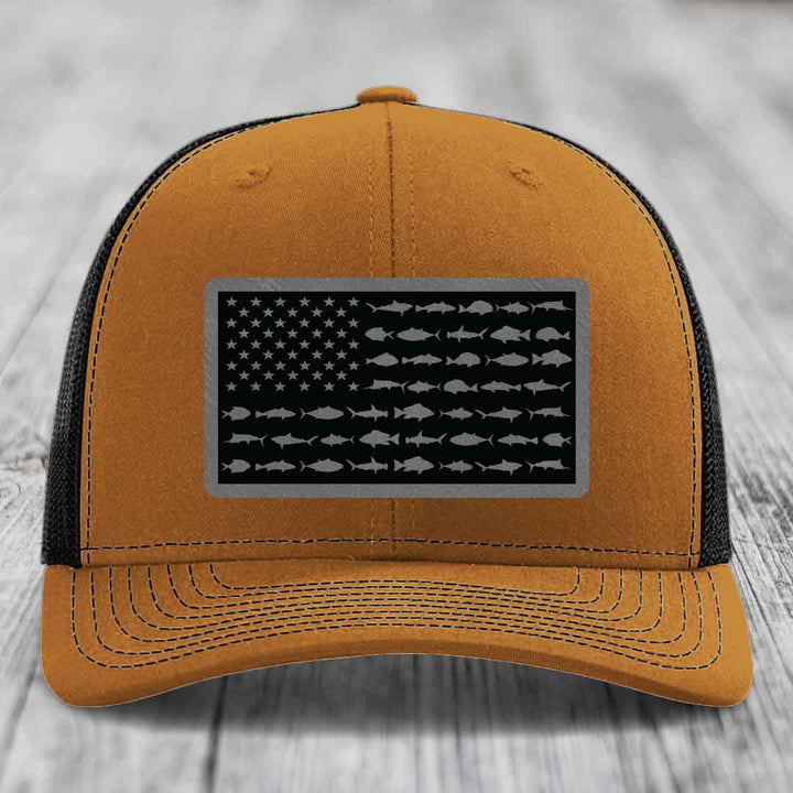 Tan trucker hat with black mesh back and gray American flag patch featuring fish silhouettes instead of stars and stripes.