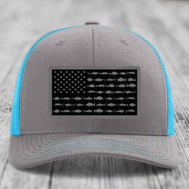 Grey trucker hat with blue mesh and stitching, featuring a black American flag patch made of saltwater fish silhouettes.