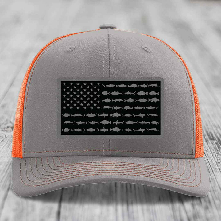 Grey trucker hat with orange mesh sides and a black leather patch featuring an American flag design made of saltwater fish silhouettes.