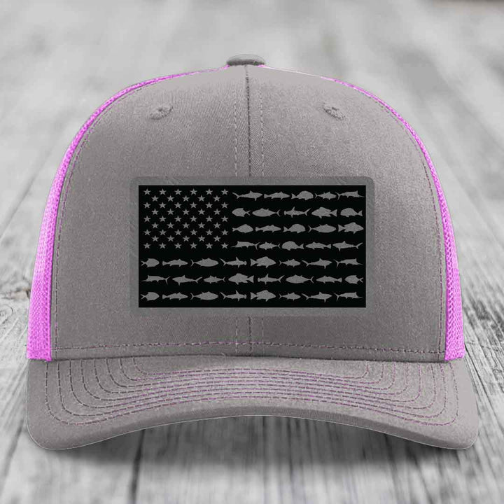 Grey trucker hat with pink mesh sides and a black leather patch featuring an American flag design made of fish silhouettes.