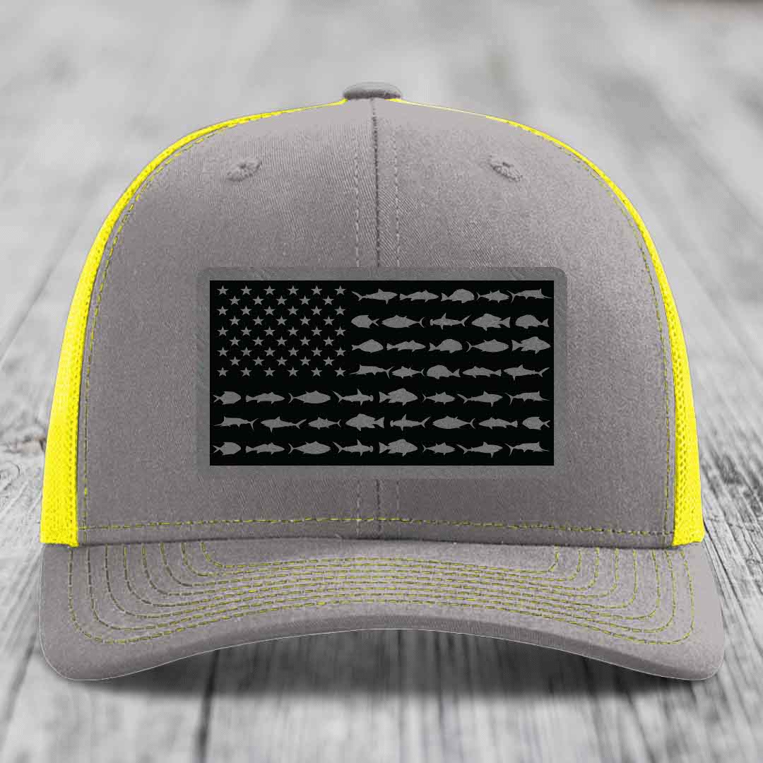 Grey trucker hat with yellow mesh and stitching, featuring a black American flag patch made of saltwater fish silhouettes.