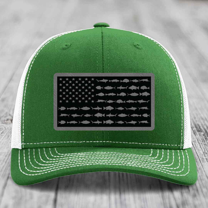 Green trucker hat with white mesh back and stitching, featuring a rectangular patch of an American flag made of saltwater fish silhouettes.