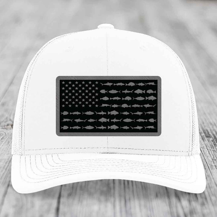 White trucker hat with black leather patch featuring American flag design made of fish silhouettes.