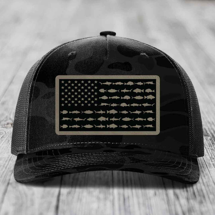 Black camouflage trucker hat with American flag patch made of saltwater fish silhouettes.