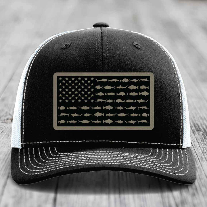 Black trucker hat with white stitching and a rectangular patch featuring an American flag design made of saltwater fish silhouettes.