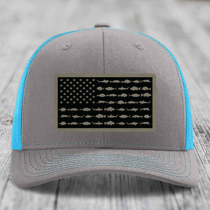 Grey trucker hat with blue mesh sides and a black leather patch featuring an American flag design made of fish silhouettes.
