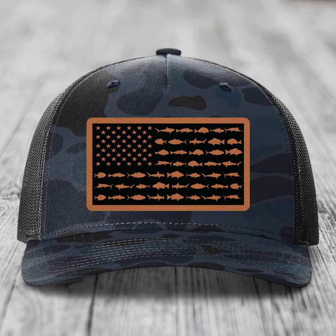 Camouflage trucker hat with American flag patch made of fish silhouettes and tan border.