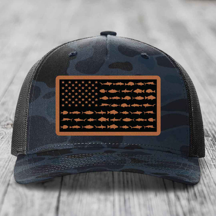 Camouflage trucker hat with American flag patch made of fish silhouettes and tan border.