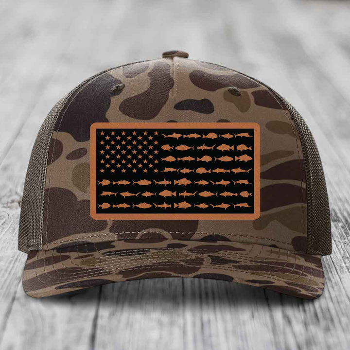 Camouflage trucker hat with American flag patch made of fish silhouettes on black background.