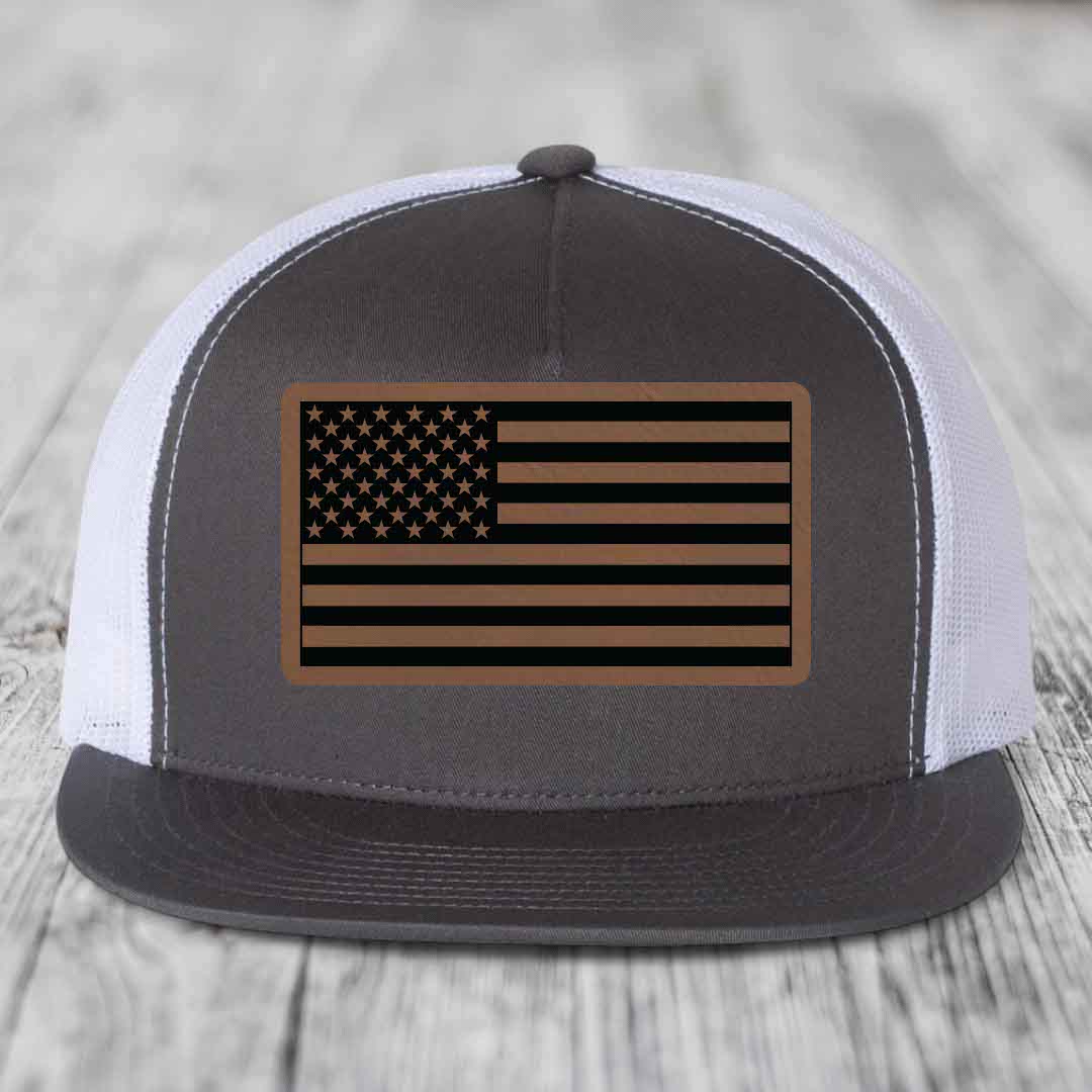 Grey front panel trucker hat with American flag leather patch, white mesh back, and grey brim.