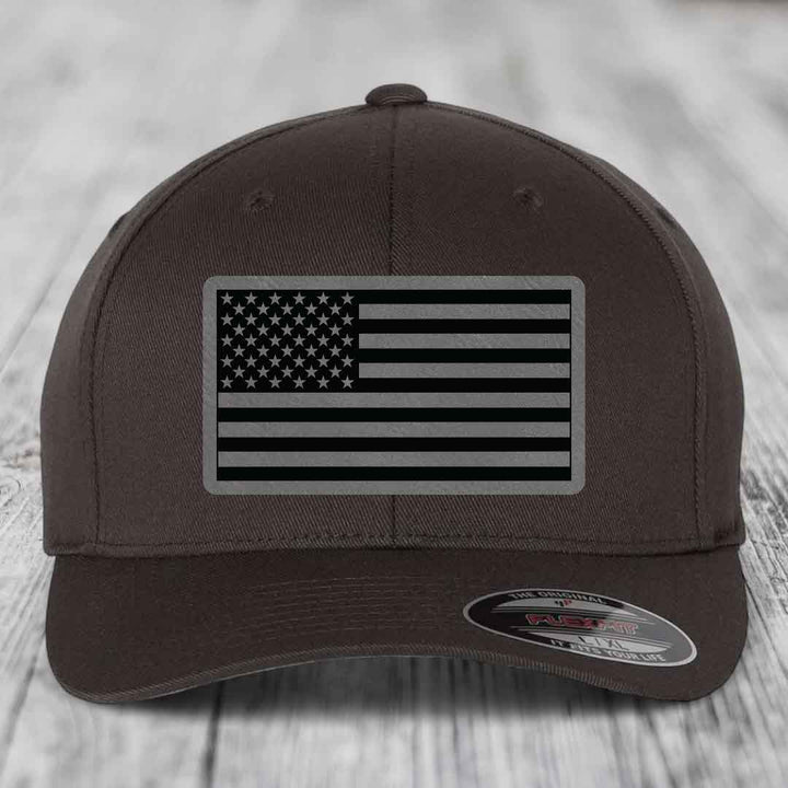 Brown baseball cap with black and grey American flag patch on front.
