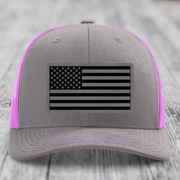Grey trucker hat with pink mesh sides and a black American flag patch on front.