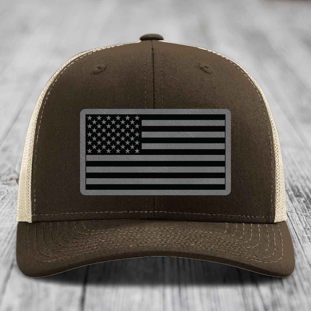 Brown trucker hat with black and grey American flag patch on front.