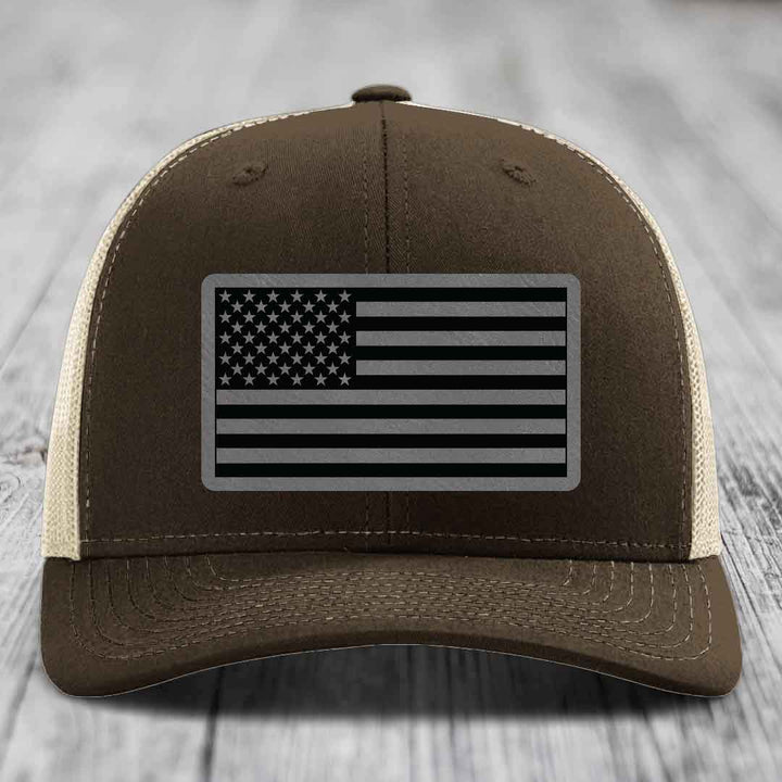Brown trucker hat with black and grey American flag patch on front.