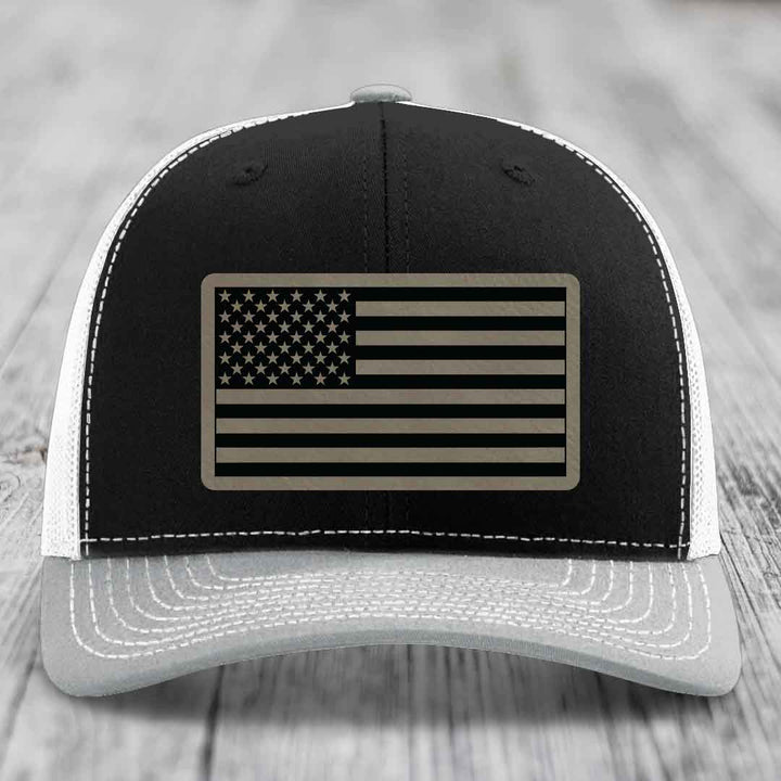 Black and white trucker hat with American flag patch on front, stitched details, gray brim.
