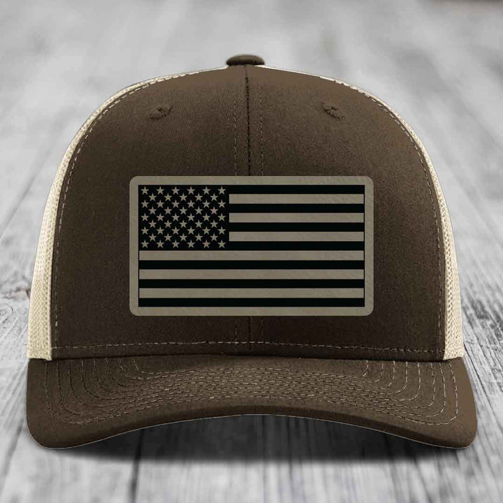 Brown trucker hat with beige mesh back and American flag patch on front.