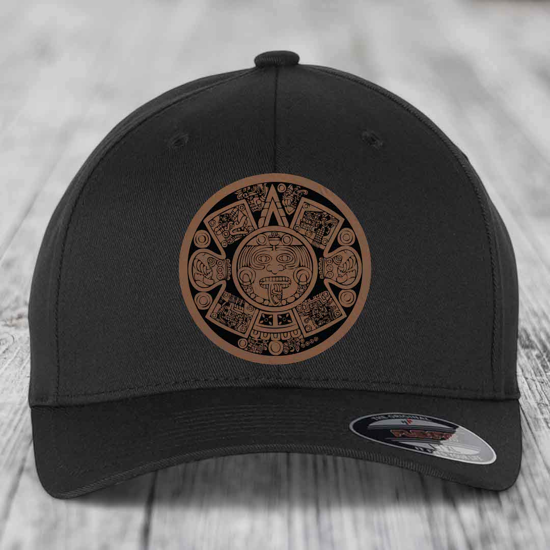 Black baseball cap with Aztec calendar patch in brown and black, on wooden surface.