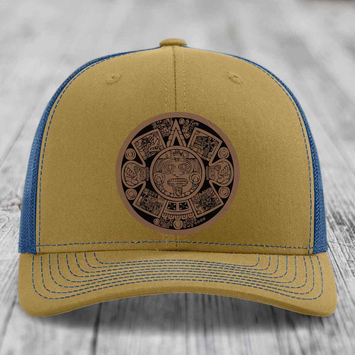 Tan trucker hat with blue mesh back and Aztec calendar leather patch on front.