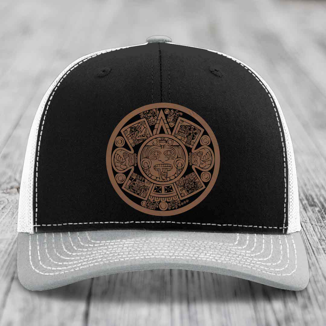 Black and grey trucker hat with brown Aztec calendar patch on front.