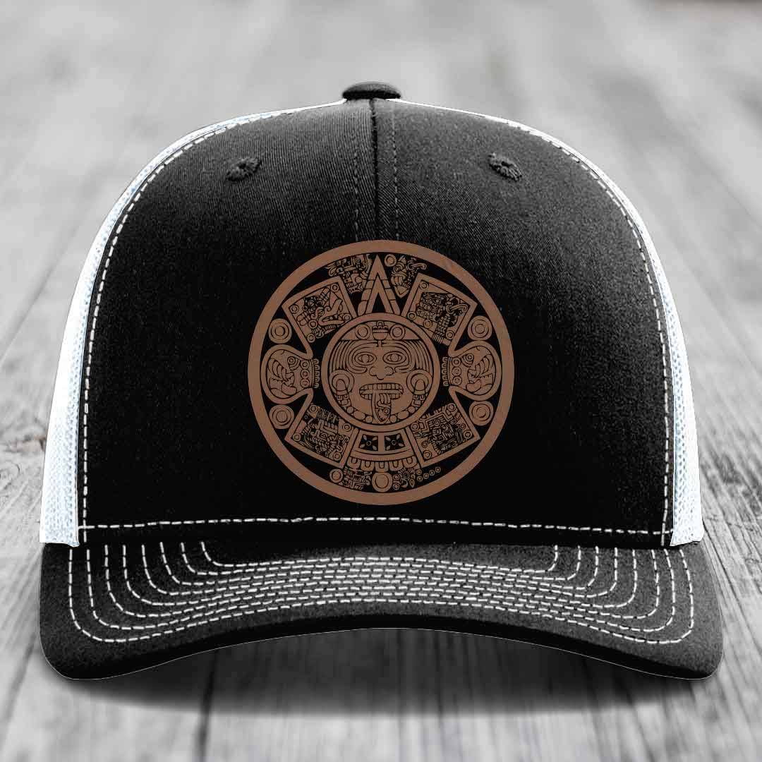 Black trucker hat with brown Aztec calendar patch and white stitching on front panel.