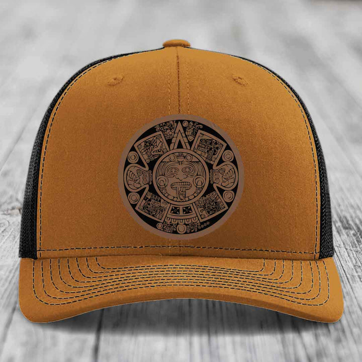 Tan trucker hat with black mesh back and Aztec calendar leather patch on front.