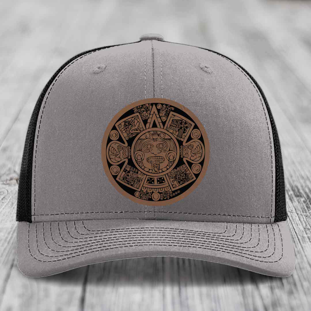 Grey trucker hat with brown Aztec calendar leather patch on front.