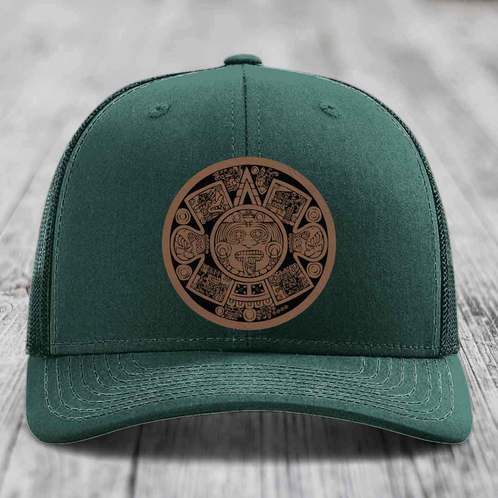 Dark green trucker hat with brown Aztec calendar leather patch on front.