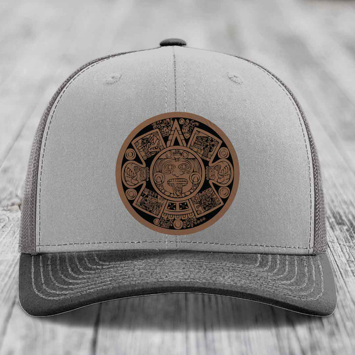 Grey trucker hat with brown Aztec calendar leather patch on front.