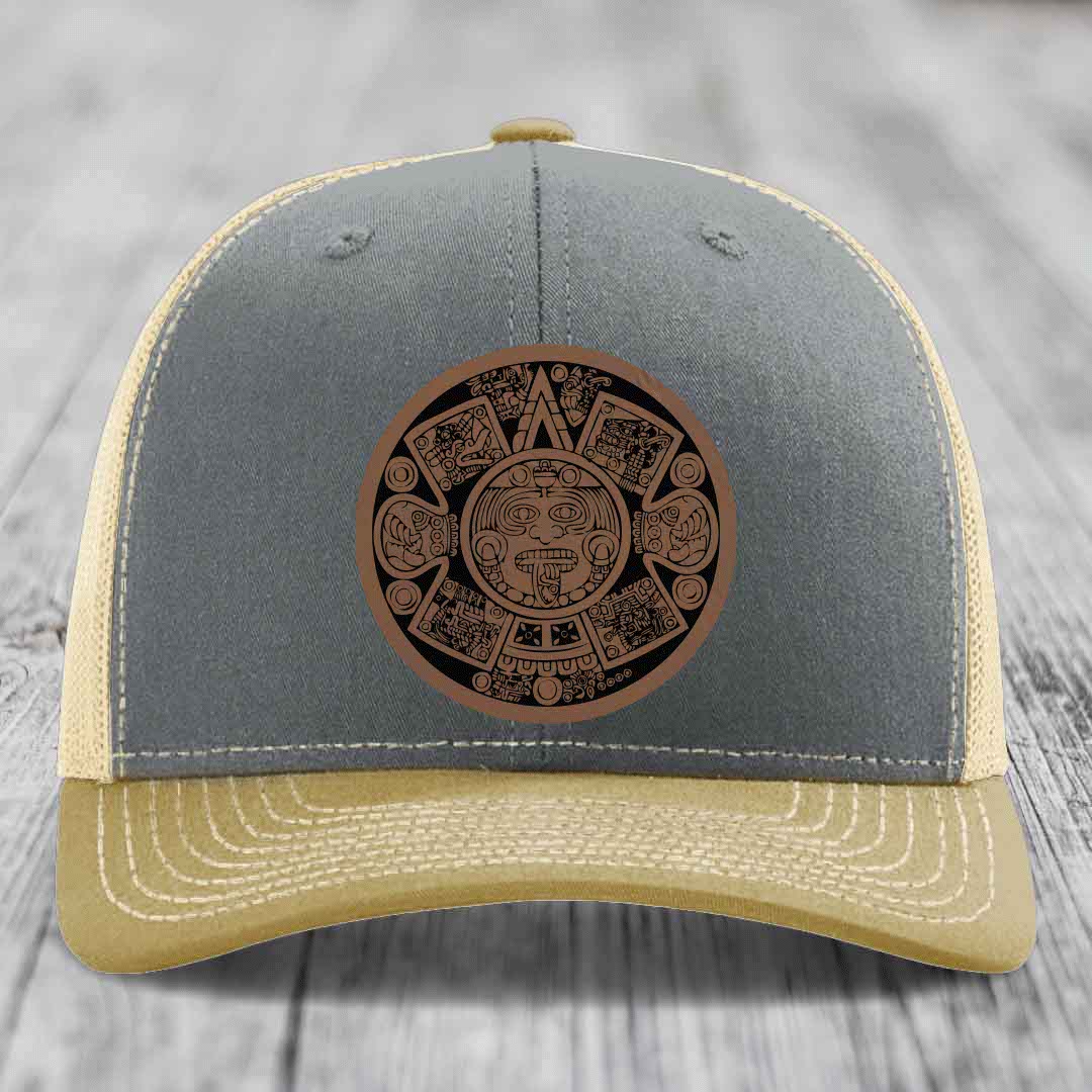 Grey and beige trucker hat with Aztec calendar leather patch on front.