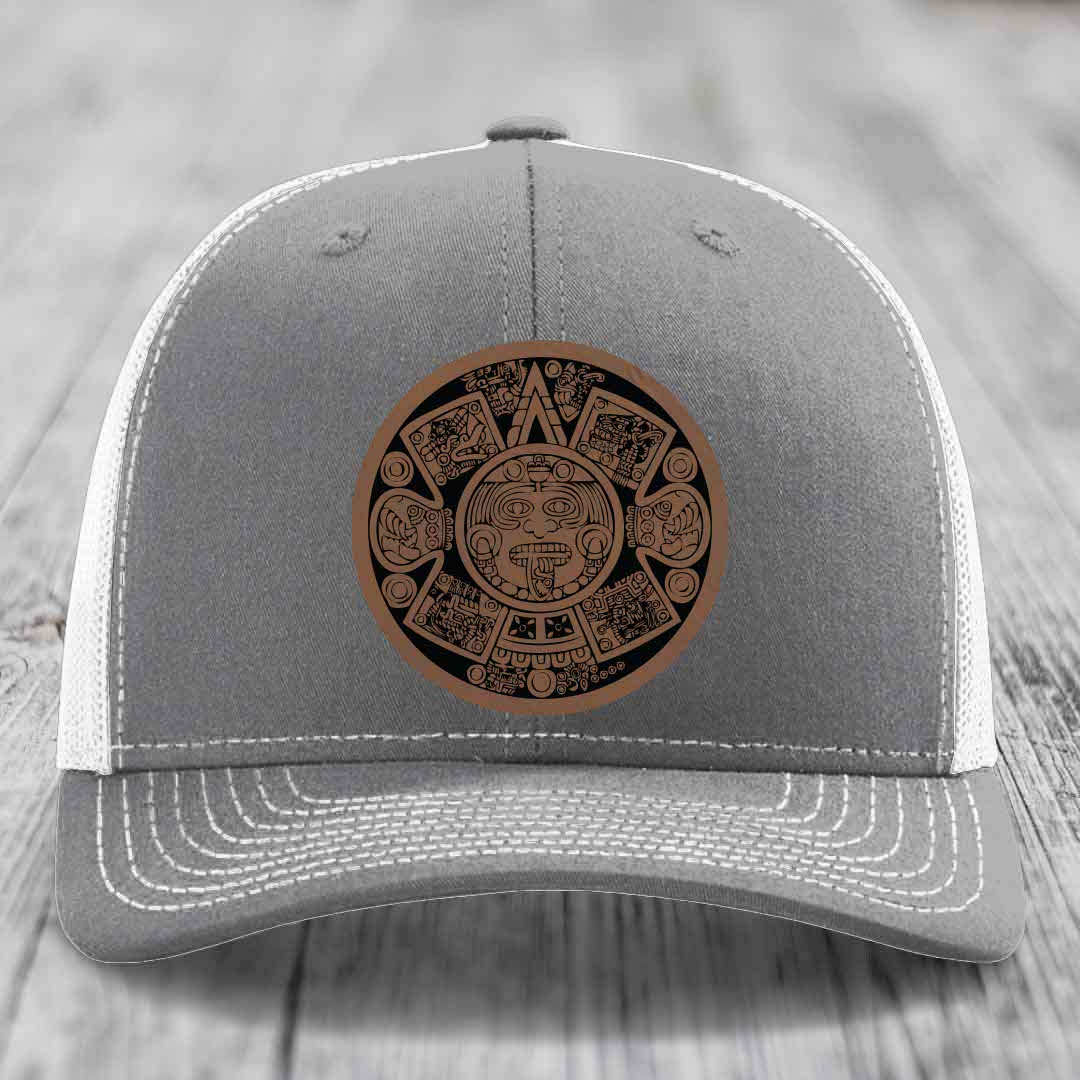 Grey trucker hat with brown Aztec calendar leather patch on front.