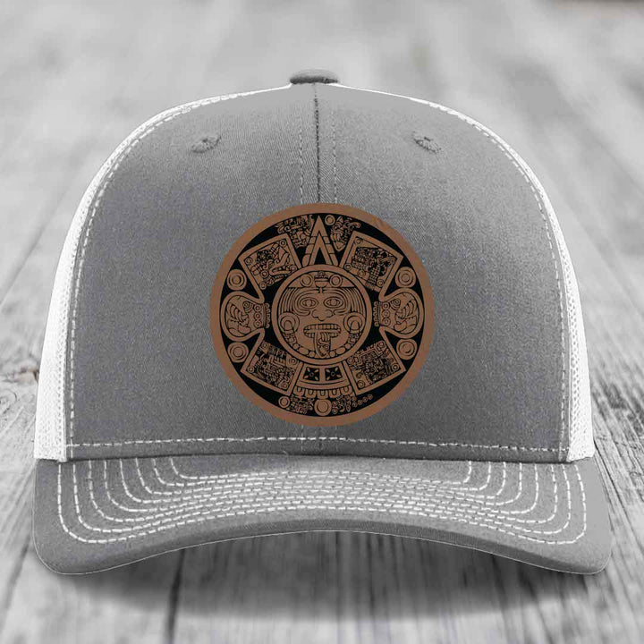 Grey trucker hat with brown Aztec calendar leather patch on front.