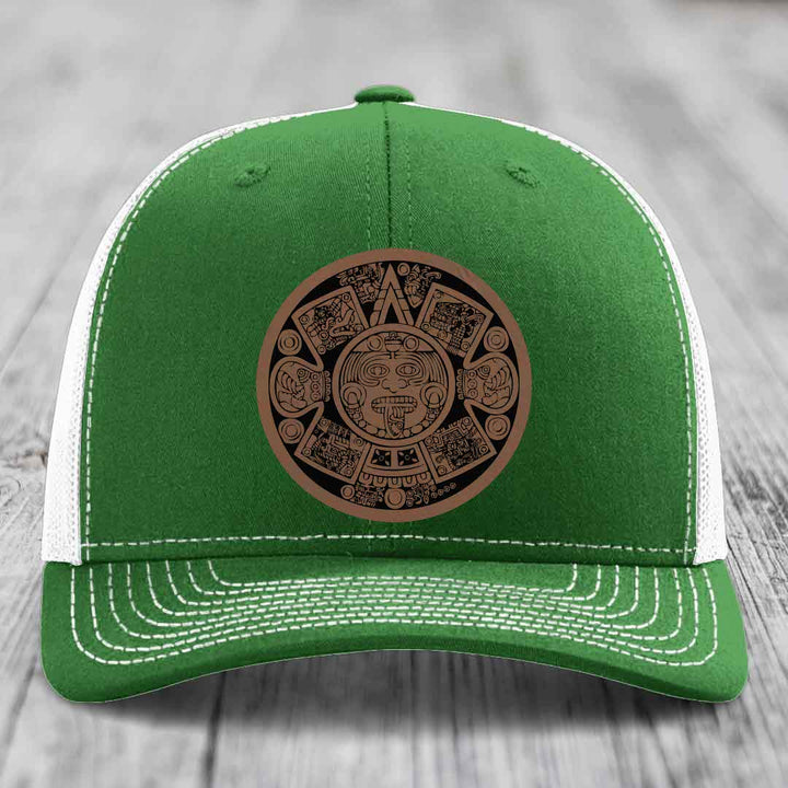 Green trucker hat with white mesh back and brown Aztec calendar leather patch on front.