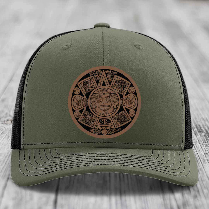 Olive green trucker hat with brown Aztec calendar leather patch on front.