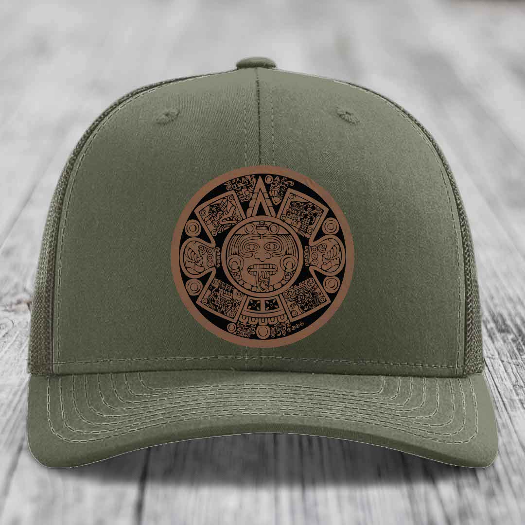Olive green trucker hat with a brown Aztec calendar leather patch on front.