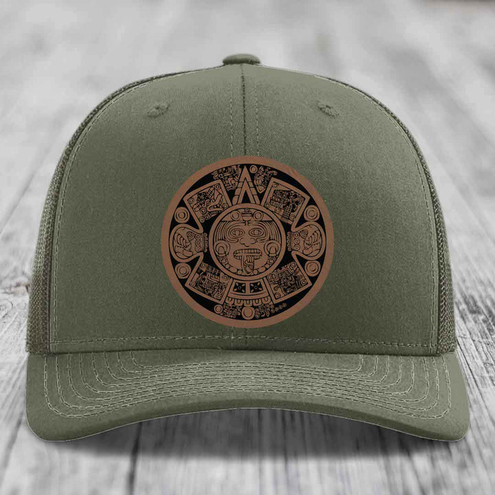 Olive green trucker hat with a brown Aztec calendar leather patch on front.