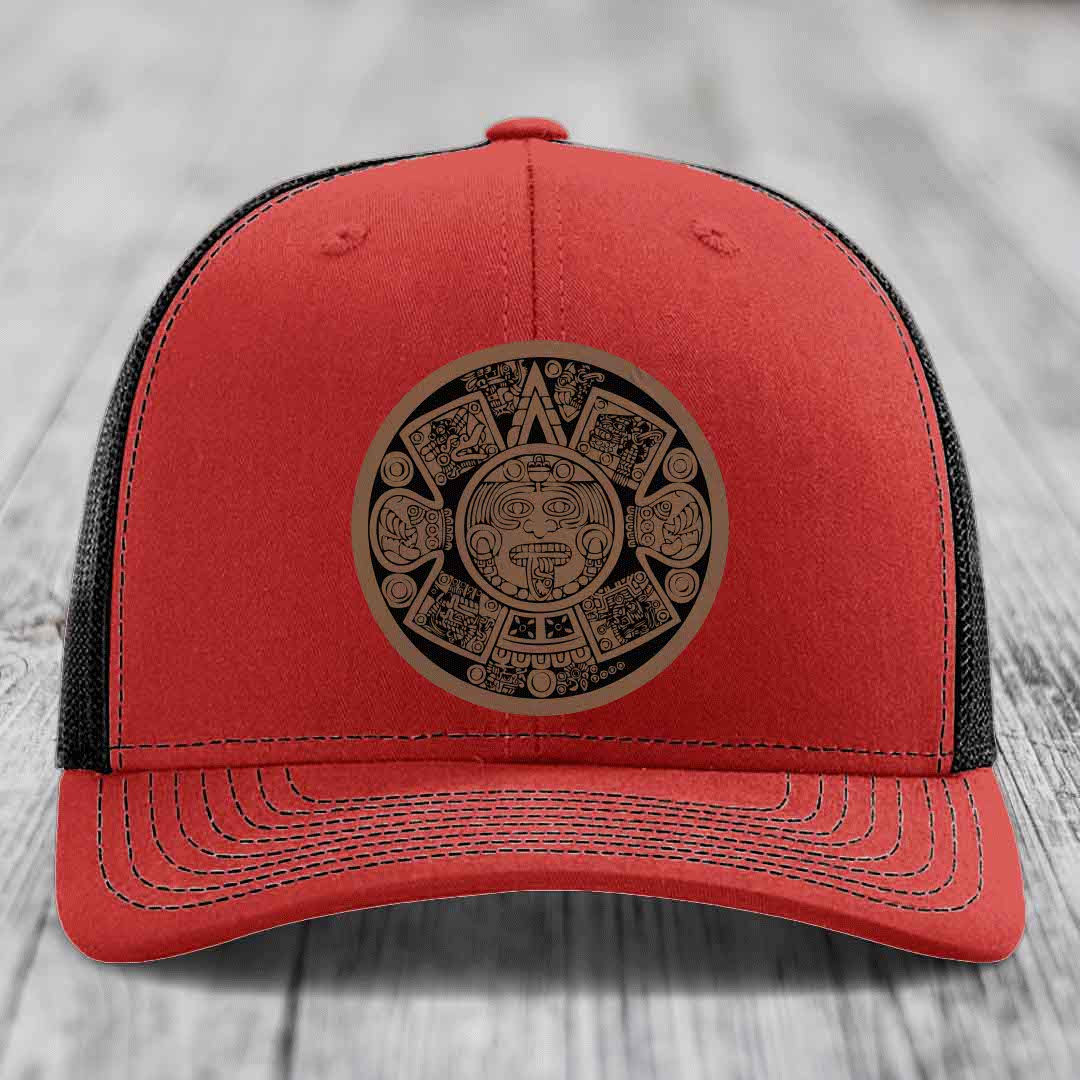 Red trucker hat with black mesh back and an Aztec calendar leather patch on the front.