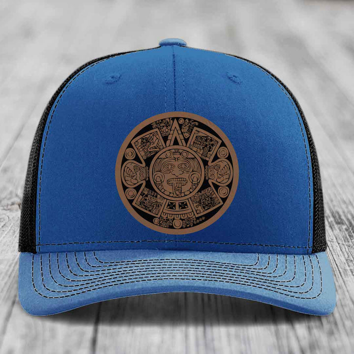 Blue trucker hat with brown Aztec calendar leather patch on front.