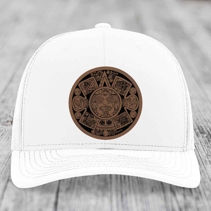 White trucker hat with brown Aztec calendar leather patch on front.