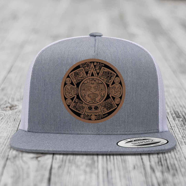 Grey trucker hat with brown Aztec calendar leather patch on front.