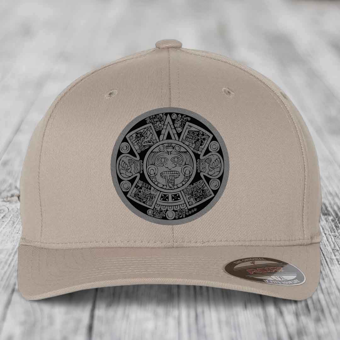 Beige baseball cap with Aztec calendar patch on front, displayed on wooden surface.
