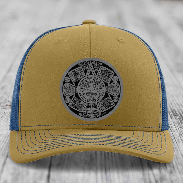Tan and blue trucker hat with Aztec calendar patch on front.