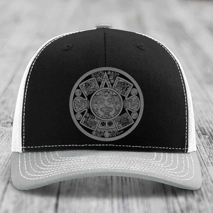 Black and grey trucker hat with Aztec calendar design on front.
