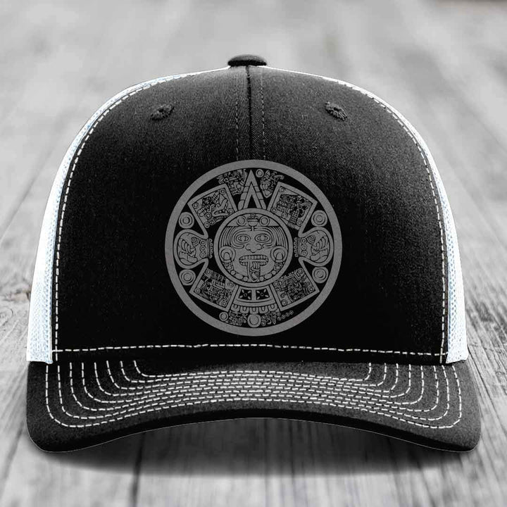 Black trucker hat with white stitching and an Aztec calendar design on the front.