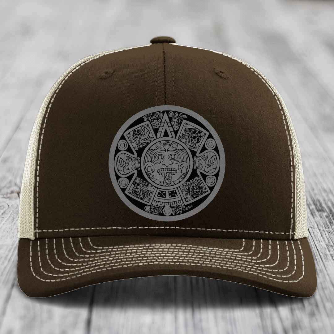 Brown trucker hat with white stitching and a grey Aztec calendar patch on front.